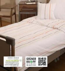 Pflegebett mit gestreifter Bettwäsche, unten die Label „OEKO-TEX MADE IN GREEN“ und „Grüner Knopf“