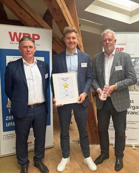 Drei Männer vor WRP-Aufstellern bei der Verleihung des WRP-Stars 2025, in der Mitte mit gerahmter Urkunde